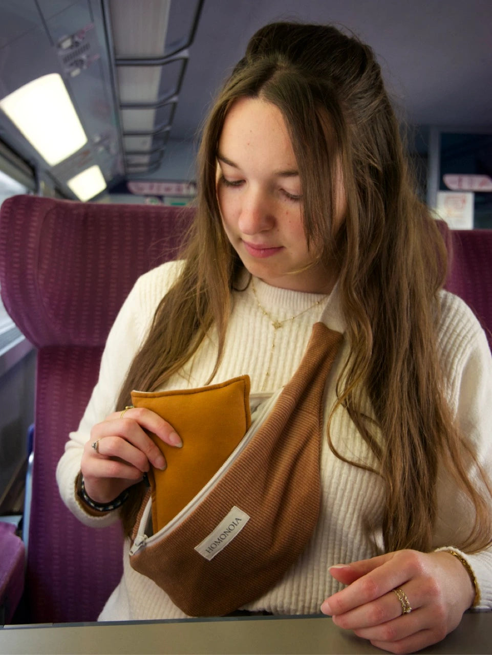 Femme voyageant en train qui utilise un petit oreiller de voyage compact et moelleux. Couleur caramel.